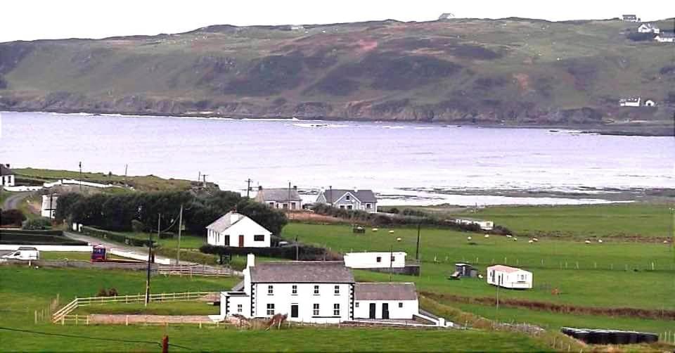a white house in a field next to a body of water at Biddy Ban’s in Carnmalin