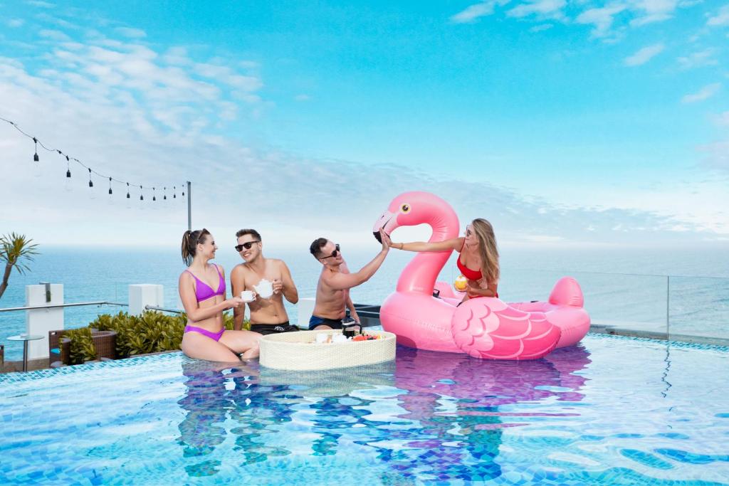 Guests gather in an infinity pool beside a large pink flamingo float with the sea behind them.