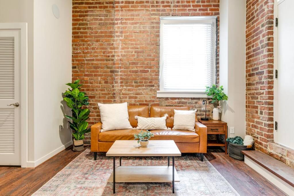 a living room with a brown couch and a brick wall at Cozy Chic Retreat in the Heart of RVA in Richmond