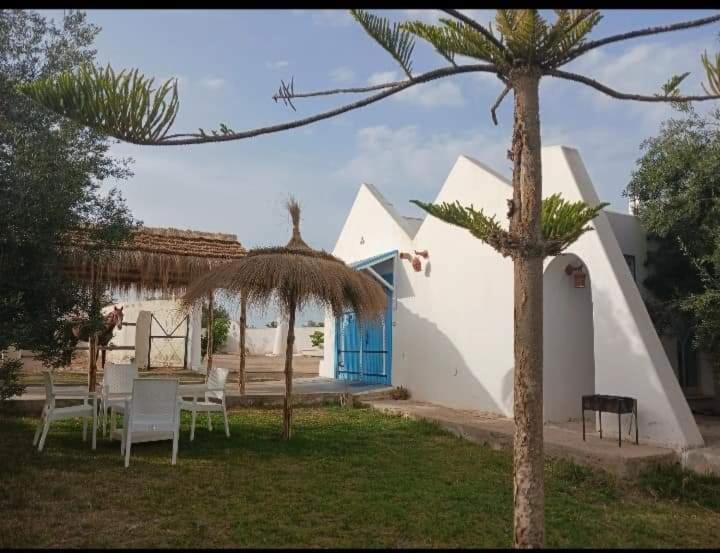 einen Garten mit Stühlen, einem Regenschirm und einem Gebäude in der Unterkunft Nouveau Bungalow Djerba in Houmt Souk