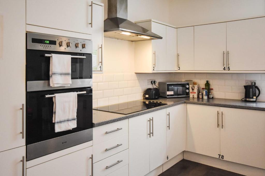 a kitchen with white cabinets and black appliances at Arlington Villas Townhouse by Clifton Short Lets in Bristol
