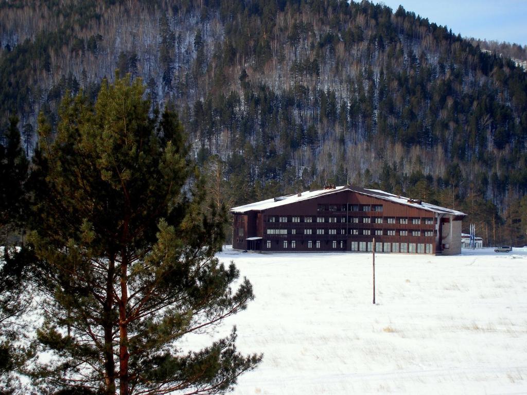 a large building in a snow covered field with a tree at Country hotel Gladenkaya in Sayanogorsk