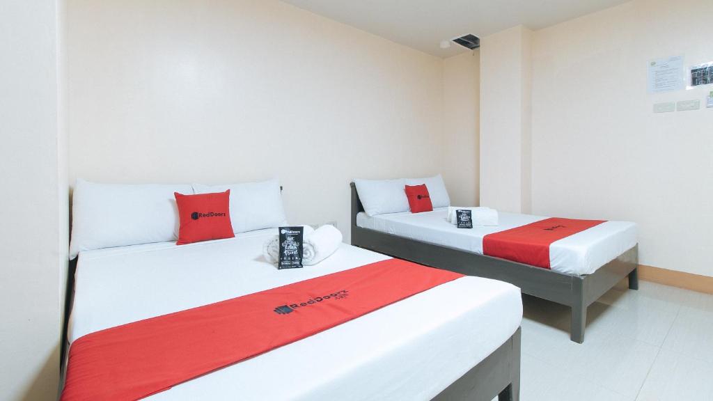 two beds in a room with red and white at RedDoorz Isabelita Hotel Tugegarao City in Tuguegarao City