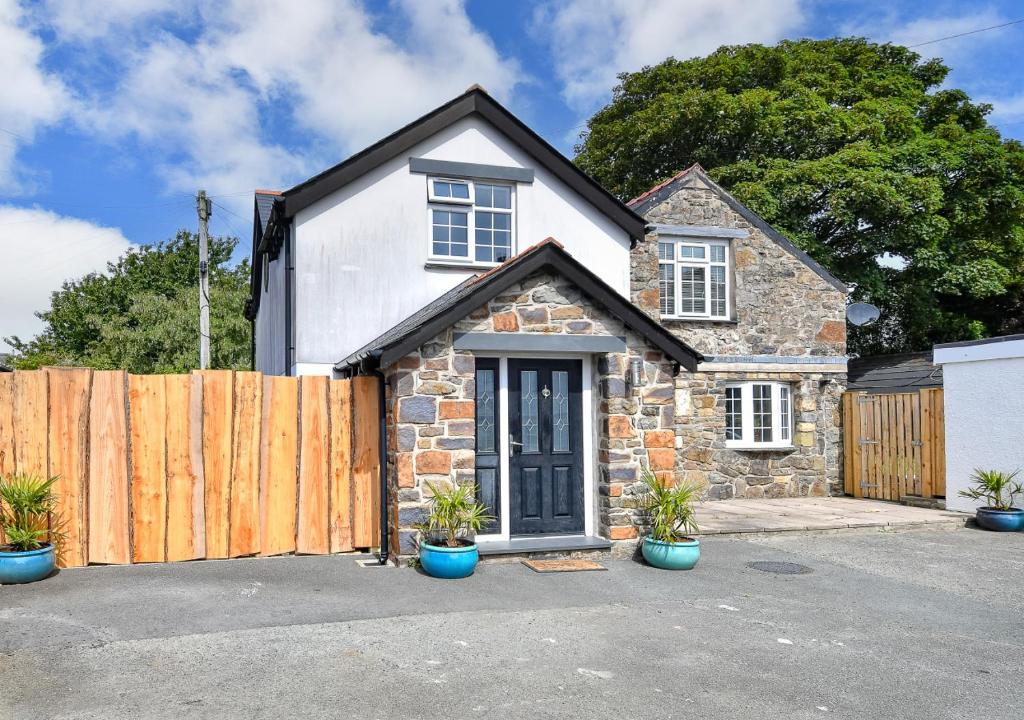 uma casa de pedra com uma cerca de madeira e vasos de plantas em Egryn Bach em Abersoch