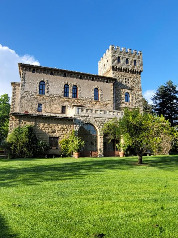 a large stone building with a grass field in front at Castello Santa Cristina in Grotte di Castro