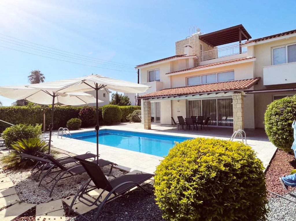 a swimming pool with chairs and umbrellas next to a house at Villa14 Sea Breeze in Khlorakas