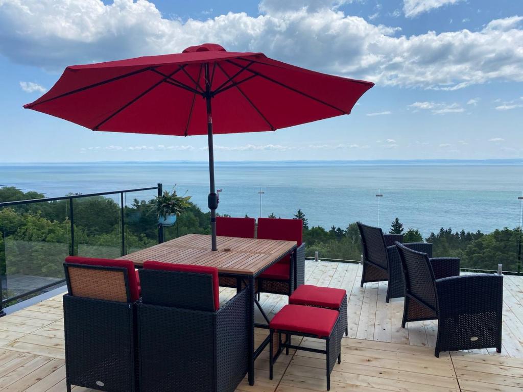 uma mesa de madeira com um guarda-chuva vermelho num deque em Maison Victoria em La Malbaie