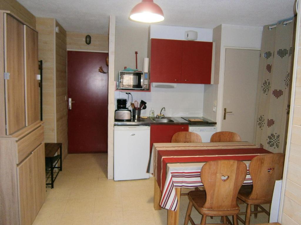 une cuisine avec une table et des chaises et une cuisine avec des placards rouges dans l'établissement Appartement confortable à Le Dévoluy 28 m² avec vue montagne, à Saint-Étienne-en-Dévoluy
