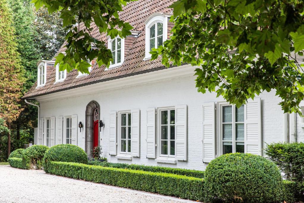 una casa blanca con una puerta roja y arbustos en La Castagnère de Bergory, en Wervicq-Sud