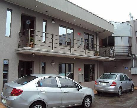 dos autos estacionados en un estacionamiento frente a un edificio en Apart Hotel Cancura, en Chillán