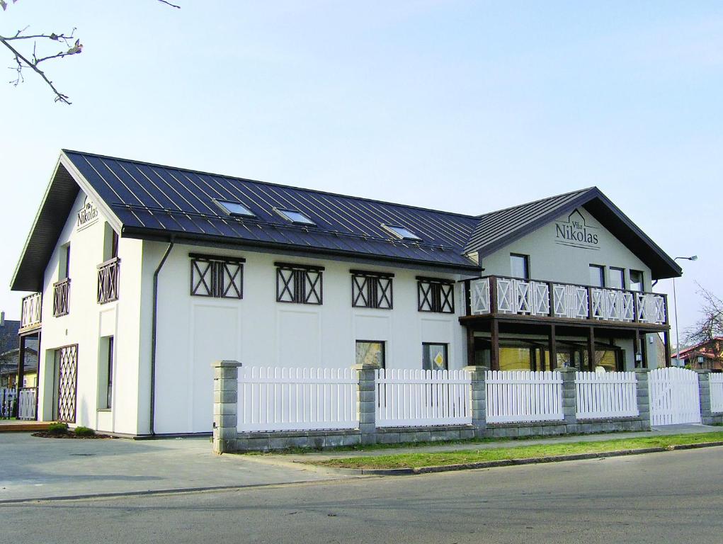 um edifício branco com um telhado preto e uma cerca branca em Vila Nikolas em Druskininkai