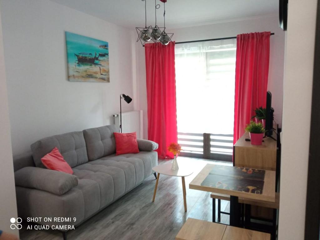 a living room with a gray couch and red curtains at Apartament ElMar in Kołobrzeg