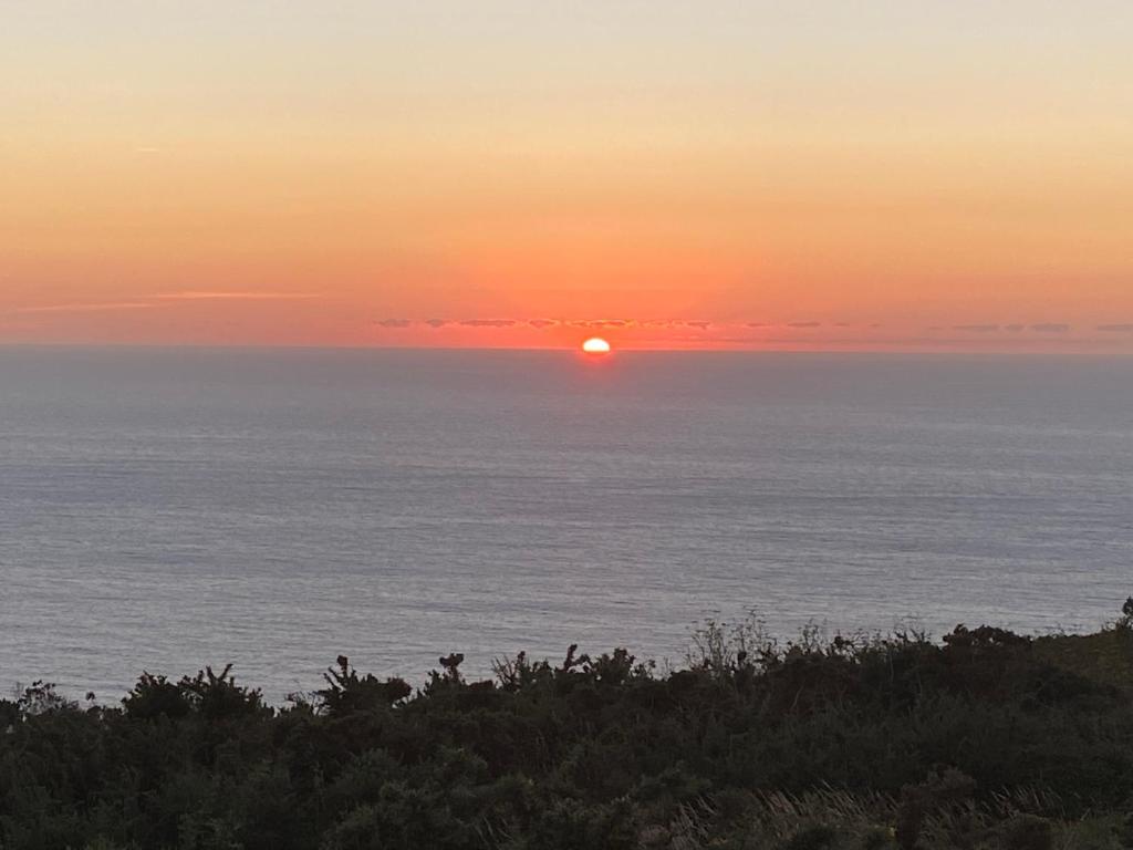 una puesta de sol sobre el océano con el sol en el cielo en Ático oceánico, en Malpica de Bergantiños
