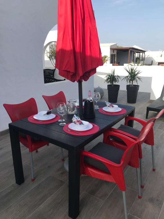 a black table with red chairs and a red umbrella at Casa Dylan in Puerto Calero