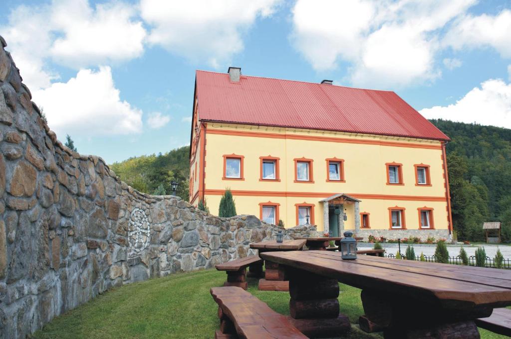 a large yellow building with a red roof next to a stone wall at Ranczo u Jana in Stronie Śląskie