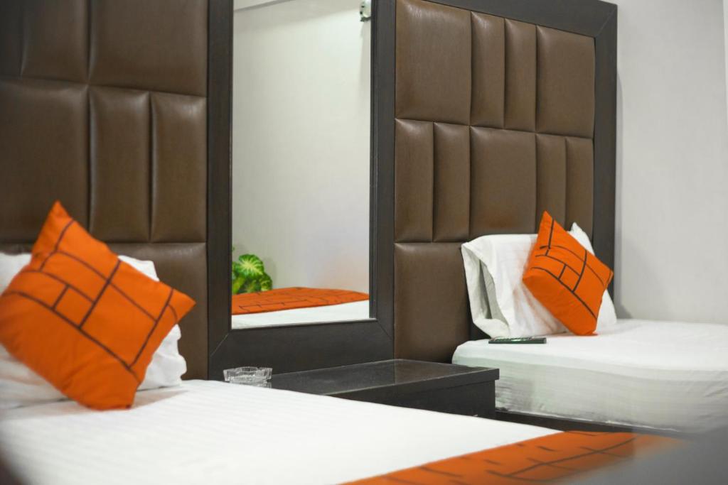 a bedroom with two beds with orange pillows and a mirror at GOHO Rooms Badar in Karachi