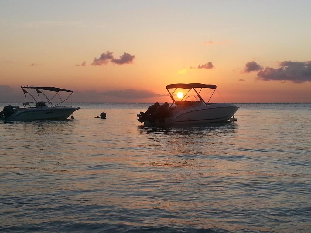 two boats in the water with the sun setting at Krishangel Beach Apartment in Flic-en-Flac