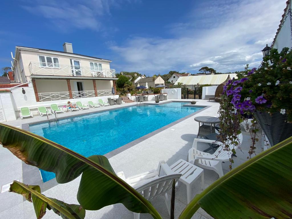 St Pierre du Bois的住宿－Beau Vallon Holiday Apartments，房屋旁的游泳池,带白色椅子