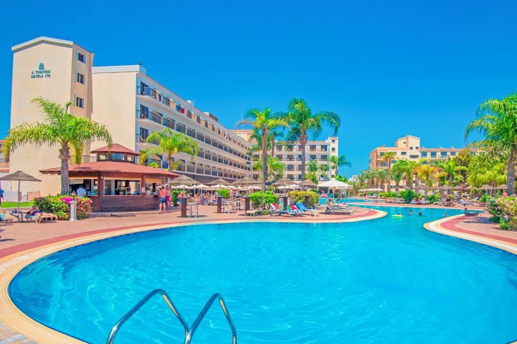 una piscina en un complejo con palmeras y edificios en Tsokkos Gardens Hotel en Protaras