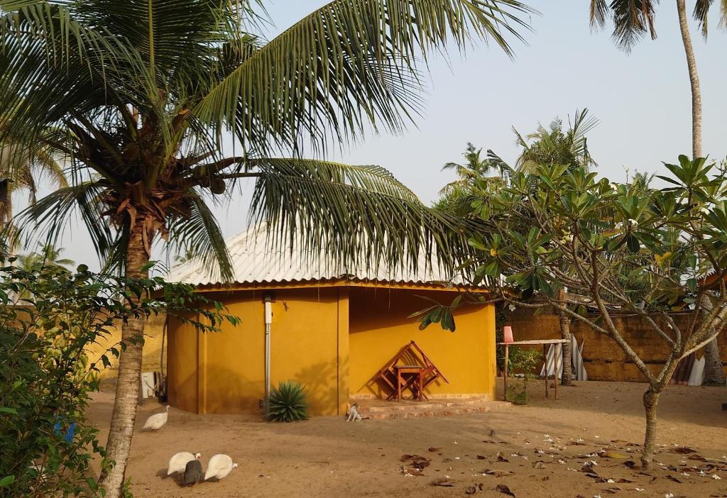a yellow house with palm trees in front of it at Rundbungalow auf Lionsrest in Grand-Bassam