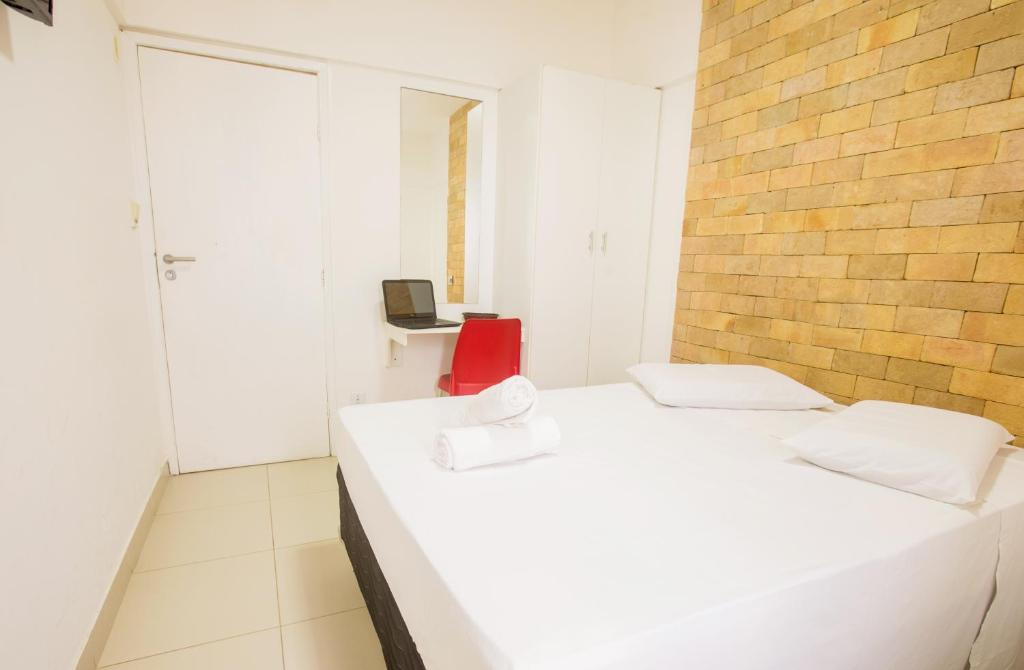 um quarto branco com 2 camas e uma cadeira vermelha em Rede Andrade Ondina Salvador em Salvador