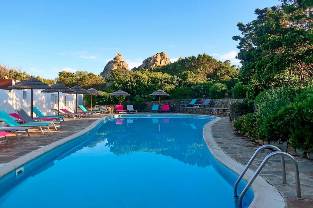 a swimming pool with chairs and umbrellas and a mountain at Domaine Bocca di Feno in Bonifacio