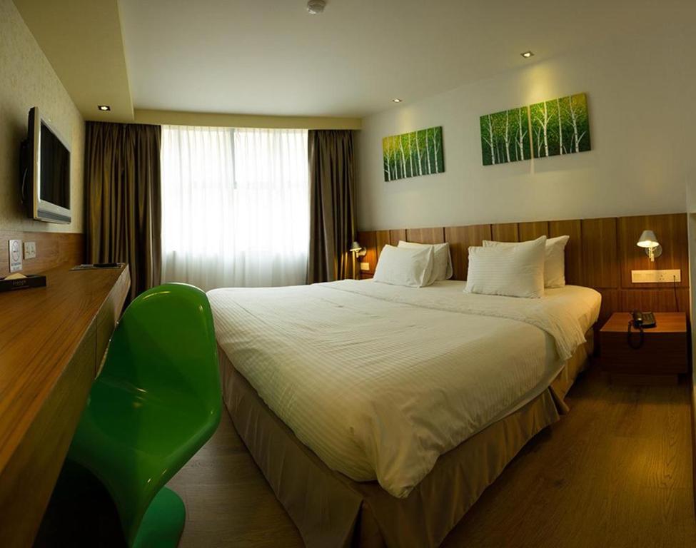 ein Hotelzimmer mit einem großen Bett und einem grünen Stuhl in der Unterkunft French Hotel in Ipoh