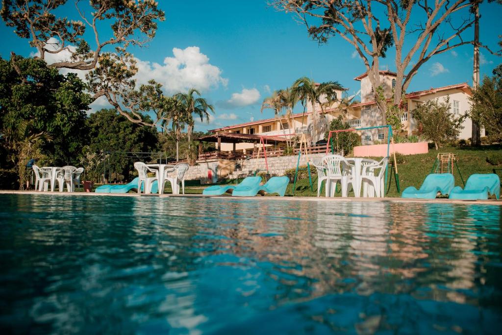 a swimming pool with blue and white chairs and trees at Pousada Solar Dona Dora in Capitólio