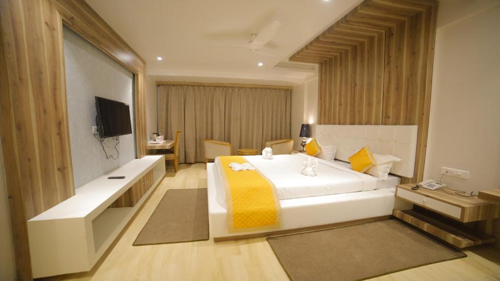 a bedroom with a large white bed and a television at Dhamma Grand Hotel Resort in Bodh Gaya