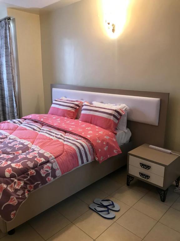 a bedroom with a bed with a red comforter and a table at Maliaways Comfy Airbnb-Jkia in Nairobi