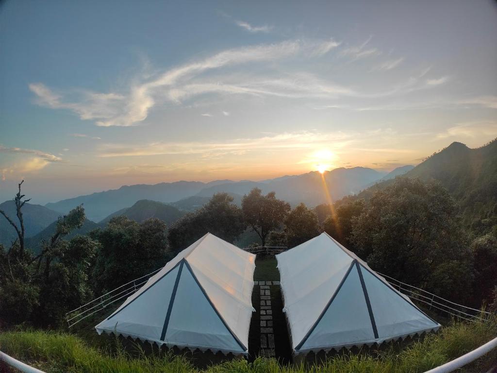 a tent sitting on top of a hill with the sunset at DugDug Camps - Glamping Amidst Nature in Bhīm Tāl