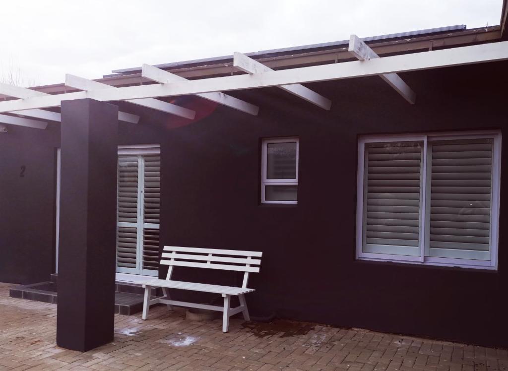 un banc blanc assis à l'extérieur d'un bâtiment noir dans l'établissement 10 Jock Meiring Guesthouse Unit 2, à Bloemfontein