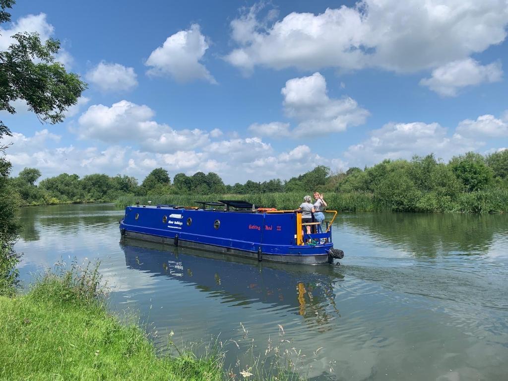 2 personnes à bord d'un bateau bleu sur une rivière dans l'établissement Narrowboat stay or Moving Holiday Abingdon On Thames DIFFERENT RATES APPLY ENSURE CORRECT RATE SELECTED, à Abingdon