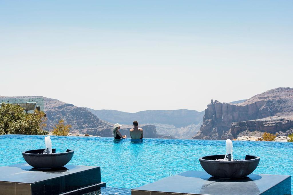 duas pessoas sentadas numa piscina de água em Anantara Al Jabal Al Akhdar Resort em Al ‘Aqar