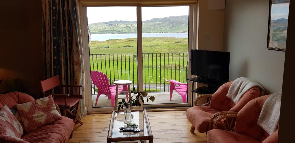 a living room with a balcony with pink chairs and a television at Beautiful 3 Bed Apartment with Balcony Sea View in Dunfanaghy