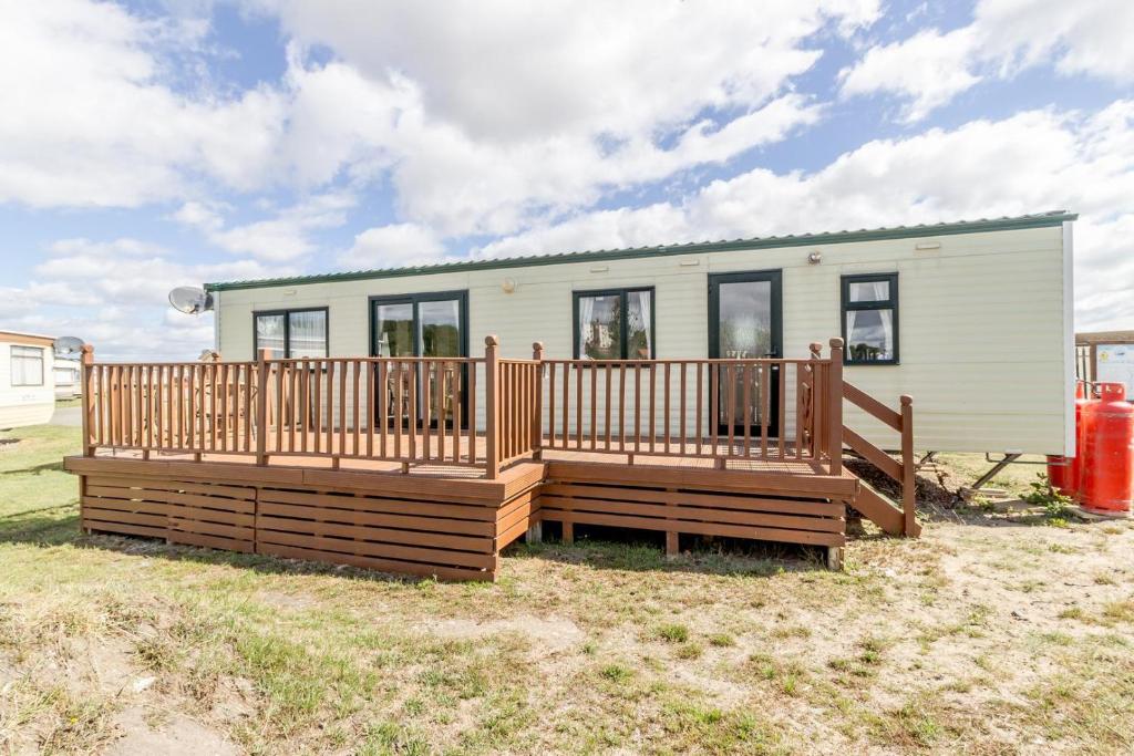 a manufactured home with a deck and a house at Great Dog Friendly Caravan For Hire At North Denes In Suffolk Ref 40068nd in Lowestoft