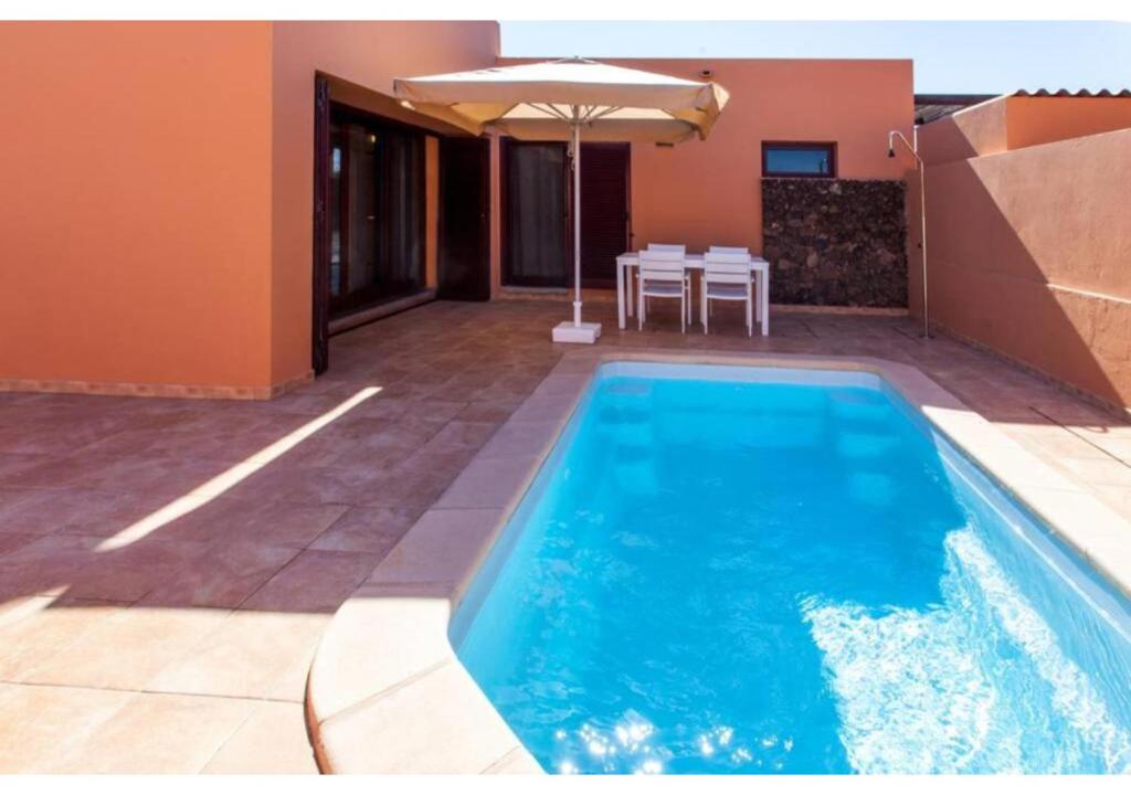 een zwembad met een parasol naast een huis bij Anahi Homes Corralejo - Villa Dracaena 2 in La Oliva