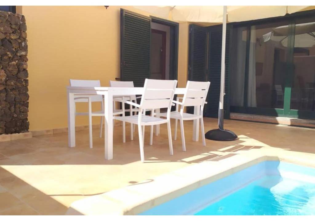uma mesa branca e cadeiras ao lado de uma piscina em Anahi Homes Corralejo- Villa Dracacena 14 em La Oliva