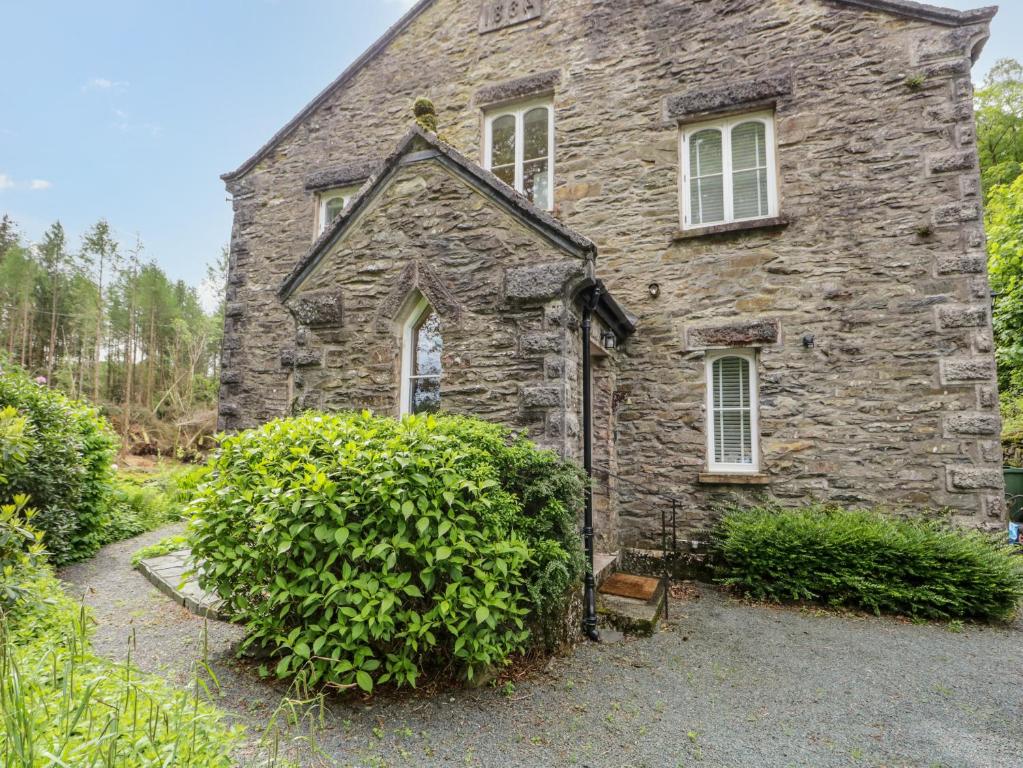 una vieja casa de piedra con arbustos delante de ella en Danes Court, en Bowland Bridge