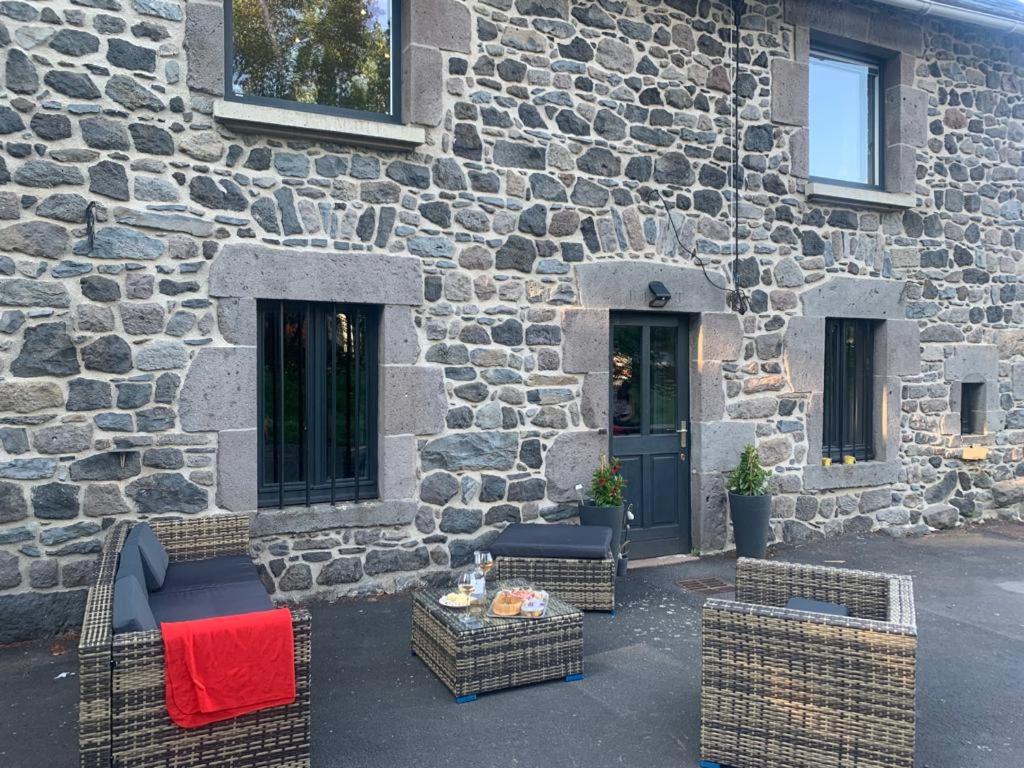 patio z wiklinowymi krzesłami i stołem przed kamiennym budynkiem w obiekcie Gîte de la Couze pavin w mieście Besse-et-Saint-Anastaise