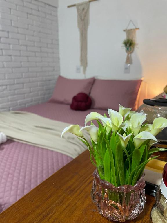 a vase of flowers on a table with a bed at Studio Baleia Franca in Imbituba