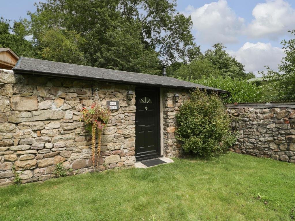 a stone shed with a black door in a yard at Shed Gwely in Abergavenny