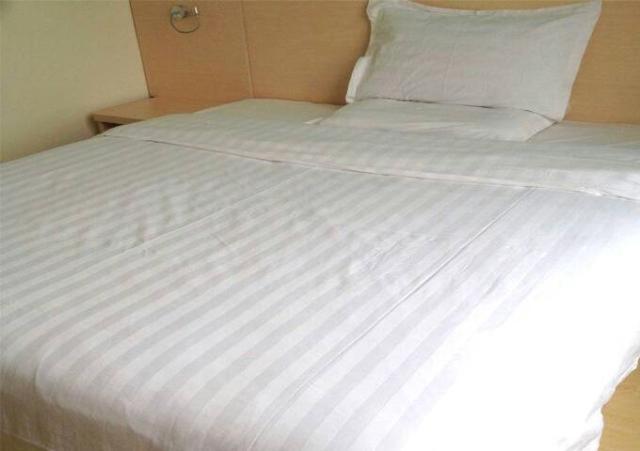 uma cama com lençóis brancos e almofadas em 7Days Inn Dushu Lake Industrial Park em Suzhou