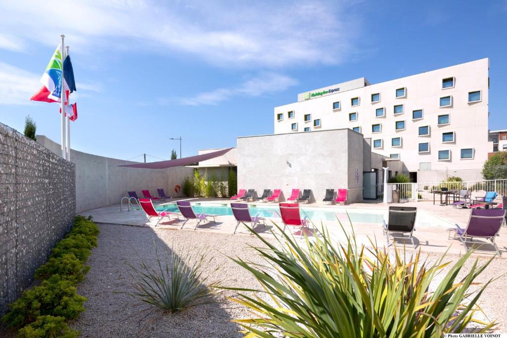 un hôtel avec une piscine, des chaises et un drapeau dans l'établissement Holiday Inn Express Montpellier - Odysseum by IHG, à Montpellier