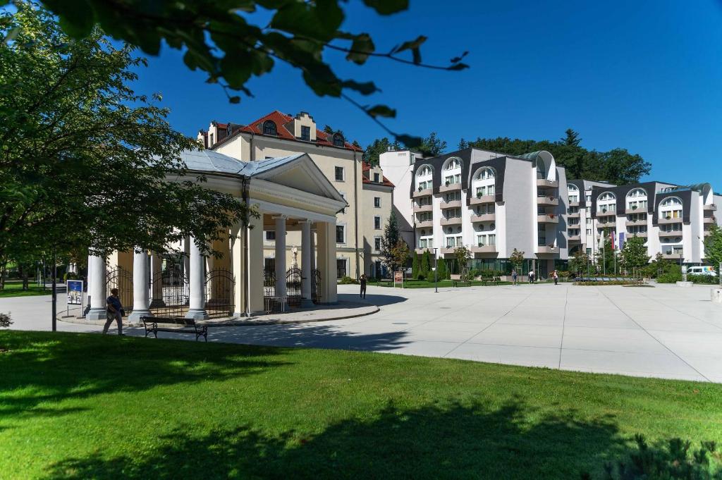 a group of buildings in a park with a bench at Grand Hotel Sava Superior in Rogaška Slatina