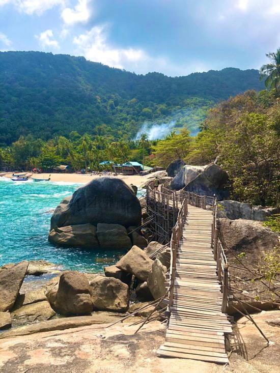 a wooden bridge over the water next to a beach at Bambu Huts in Baan Tai