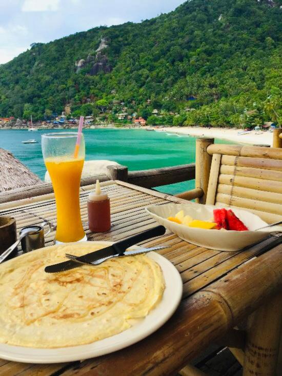 a table with a plate of food and a drink at Bambu Huts in Baan Tai