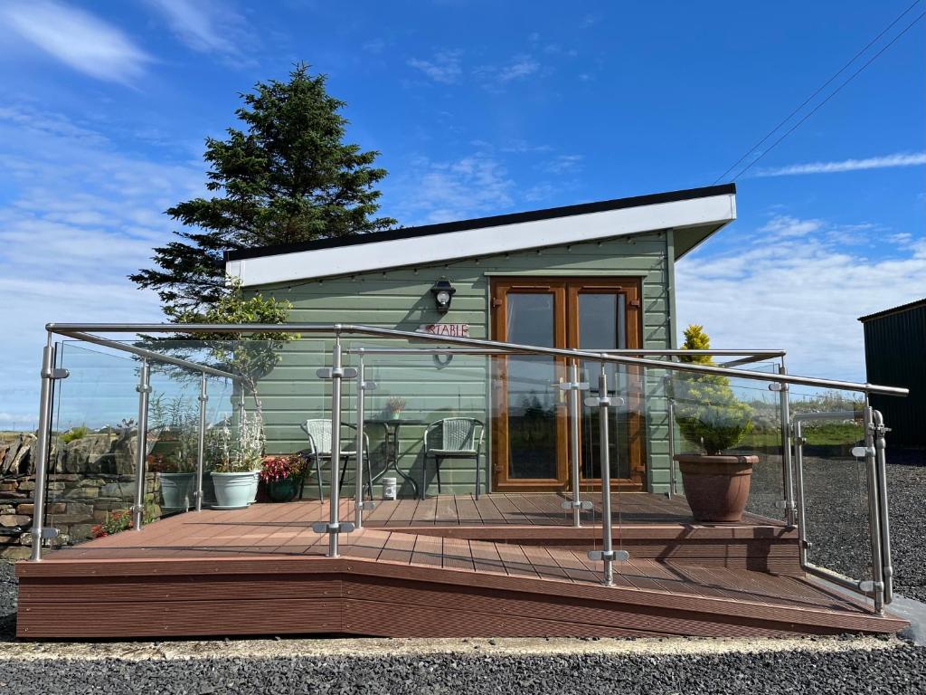 una pequeña casa verde con una gran terraza de madera en The Stable - NC500, en Wick