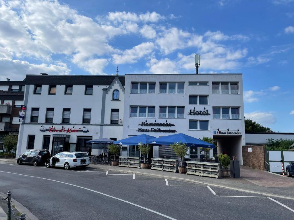 un grand bâtiment blanc avec des parasols bleus dans un parking dans l'établissement Hotel Fassbender, à Pulheim