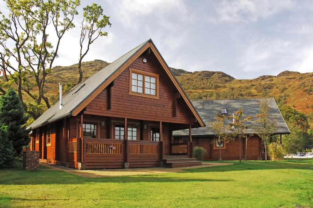 a large wooden house with mountains in the background at Ardlui Lochside Lodges in Ardlui